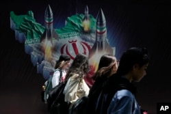 Iranian women without a mandatory head scarf, or hijab, walk past a banner in Tehran in April.